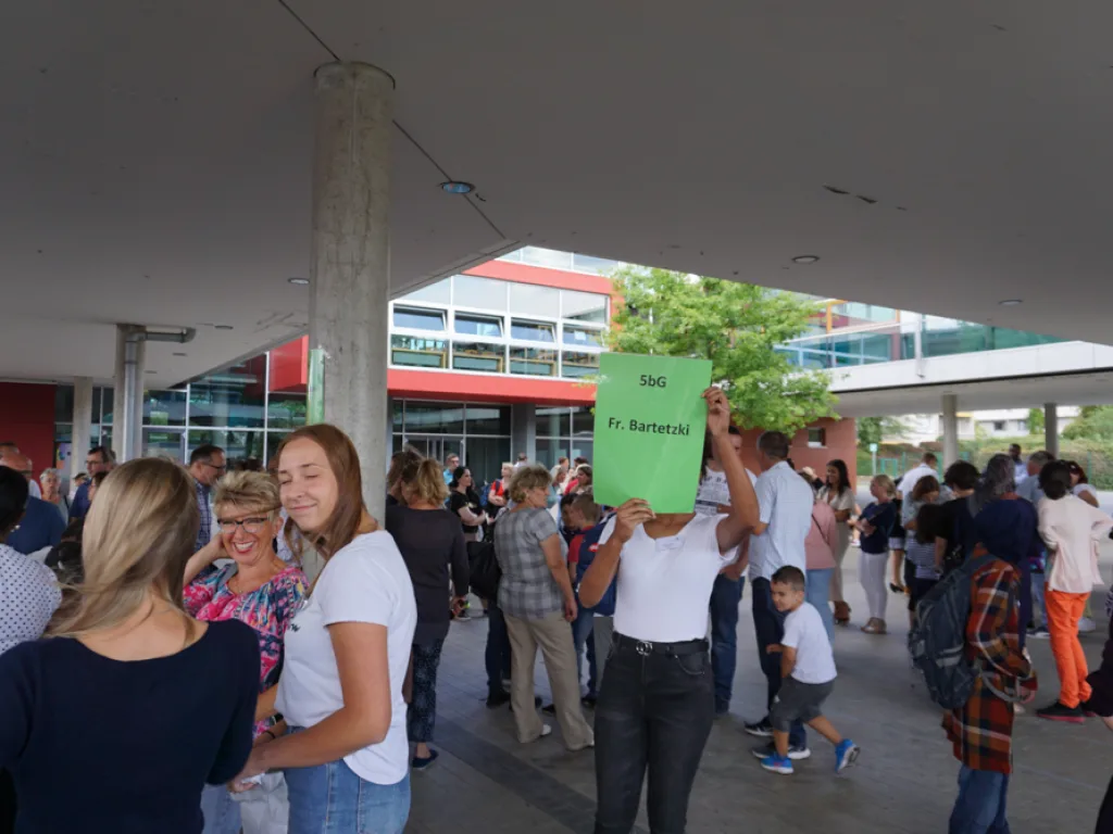 Familien stehen auf dem Schulhof, eine Person hält ein grünes Klassenschild.